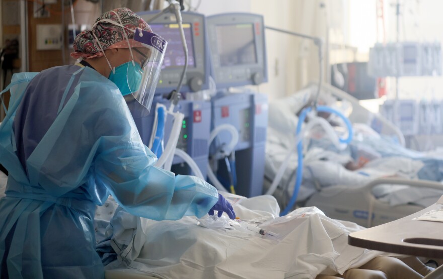 Hospital workers in blue surgical gowns, gloves and face masks care for intubated patients.