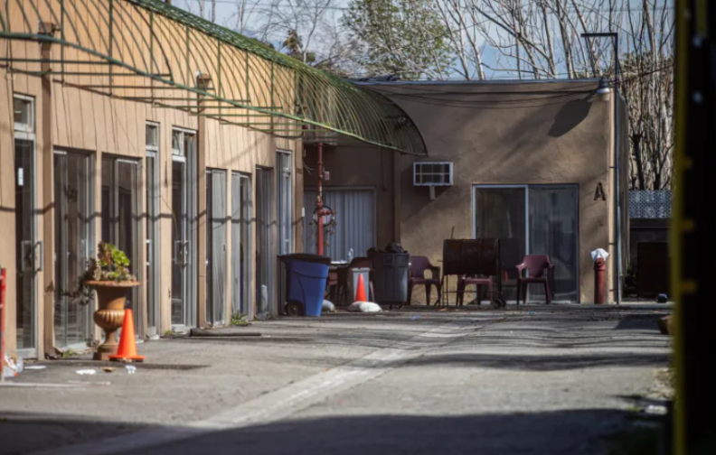 The outside of a building is seen with an alleyway leading to multiple doors. There is multiple trash cans outside of the buidling.