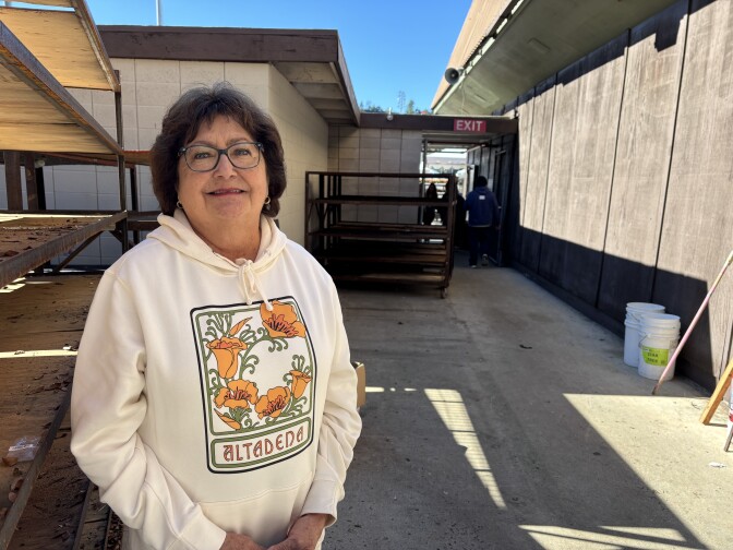 A woman wearing an Altadena hoodie stands in a work area, and smiles for the camera. 