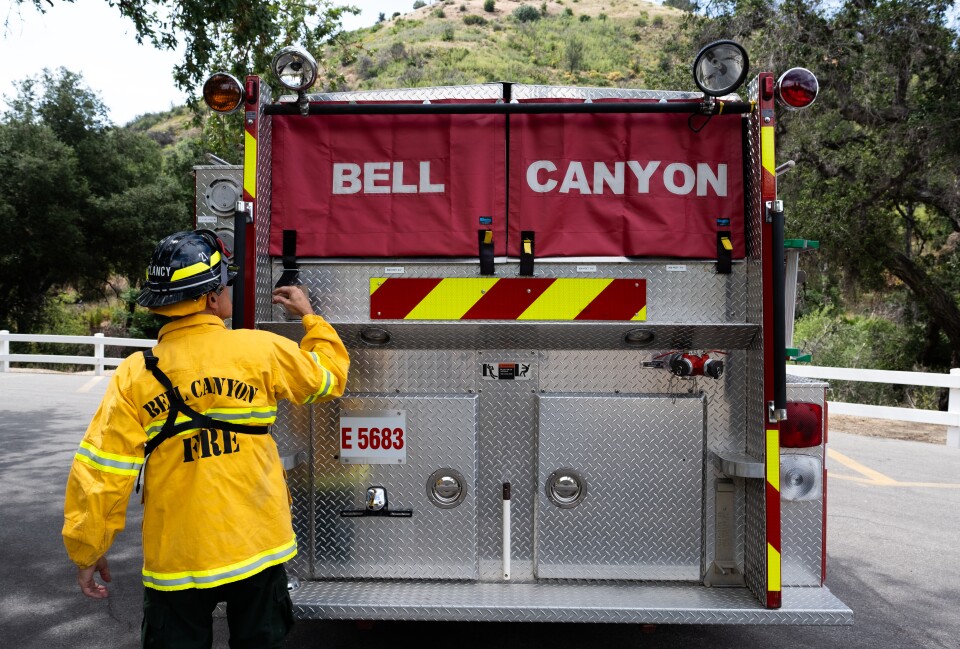 A man in a yellow jacket and a helmet stands next to a truck with red and silver.