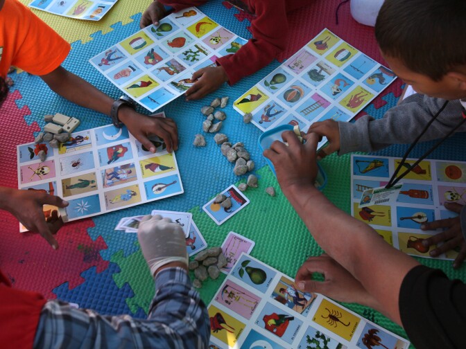 Tijuana, BAJA CALIFORNIA, Mexico - December 16:   At the El Barretal shelter in Matamoros, Tijuana, children play listeria with one of the workers at the Save the Children tent.

 In Tijuana, Mexico, children members of the migrant caravan are learning to live in limbo as they move between shelters, settling in as much as possible to create a sense of normalcy, with help from NGOs, counselors and aid organizations. (Photo by Peggy Peattie)