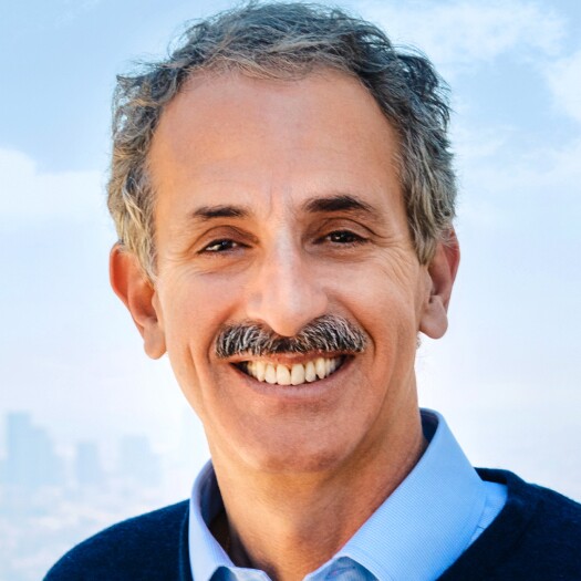Headshot of Mike Feuer. He's smiling and wearing a blue collared shirt and dark sweater or jacket. He has gray wavy hair and a mustache and a light complexion.