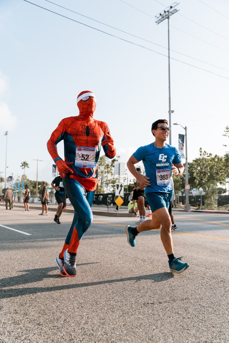 Person in Spider-man costume and man in blue short and shirt running.