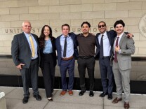 Six people stand in front of a federal courthouse in downtown Los Angeles.