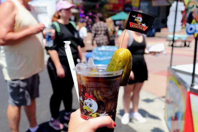 A "Charlie's Chicken" Dr. Pepper is held up in front of a crowd of OC Fair people.