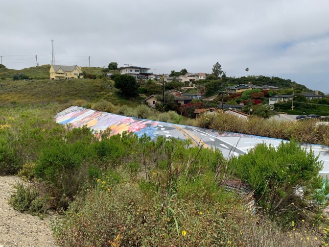 A mural has been painted along a stretch of concrete. There are pretty flowers, and black-and-white roadways painted along it, a nod to both the land and busy La Cienega Boulevard. 