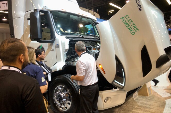 People gather around a large, white electric semi-truck that has it's hood open. 