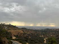 A bolt of lightning hits the ground in the distance with the distinctive dome of the Griffith Observatory visible in the hills at left.