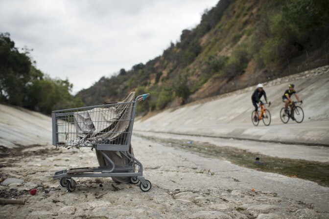 Bicyclists ride the Arroyo Seco trail on Tuesday morning, May 5, 2015 where several encampments line the riverbed.