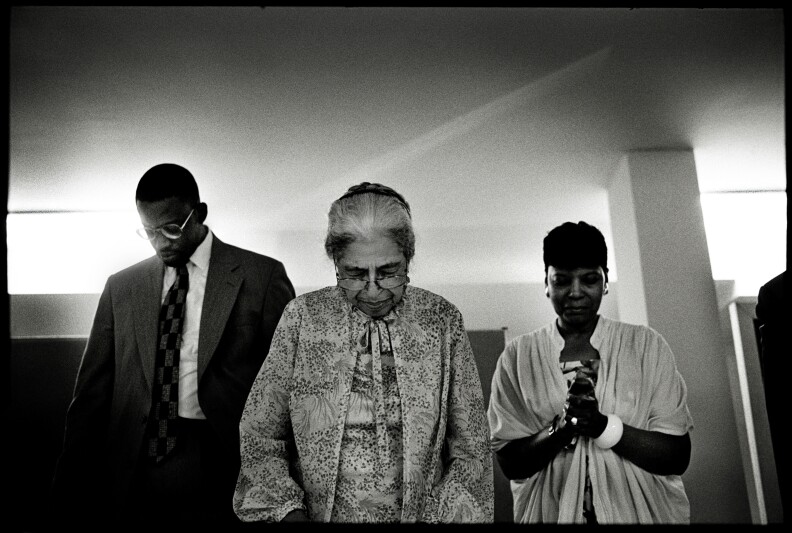 Three people stand with their heads bowed in prayer.