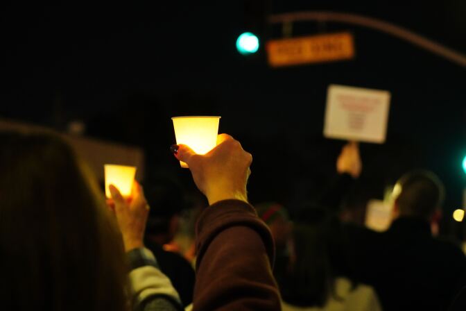  Hands holding up small lights at what appears to be a protest at night. 
