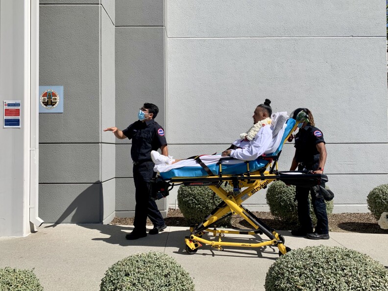 An Asian man is being transported by stretcher by two EMT's.