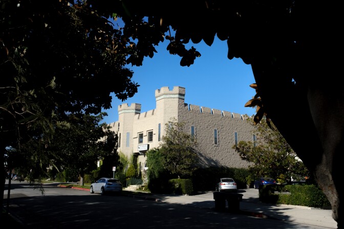 An exterior of a home that resembles an ancient castle in Burbank. The light-colored building with two turrets is seen from a distance, framed by tree branches.