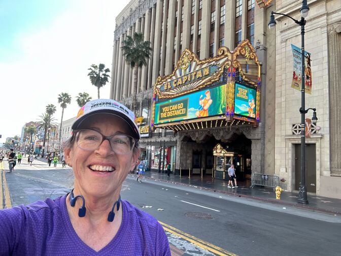 A woman with glasses smiling in front of a vintage movie theater. 