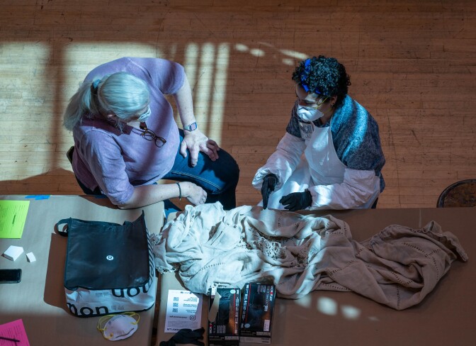 Margalit Schindler consults with a local Angeleno about how to safely clean a beloved hand-woven curtain that hung in a house with severe smoke damage from the Eaton Fire. The curtain is white. The Angeleno wears a blue polo style shirt. 