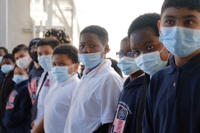 A row of students, all wearing polo shirts and blue surgical masks.