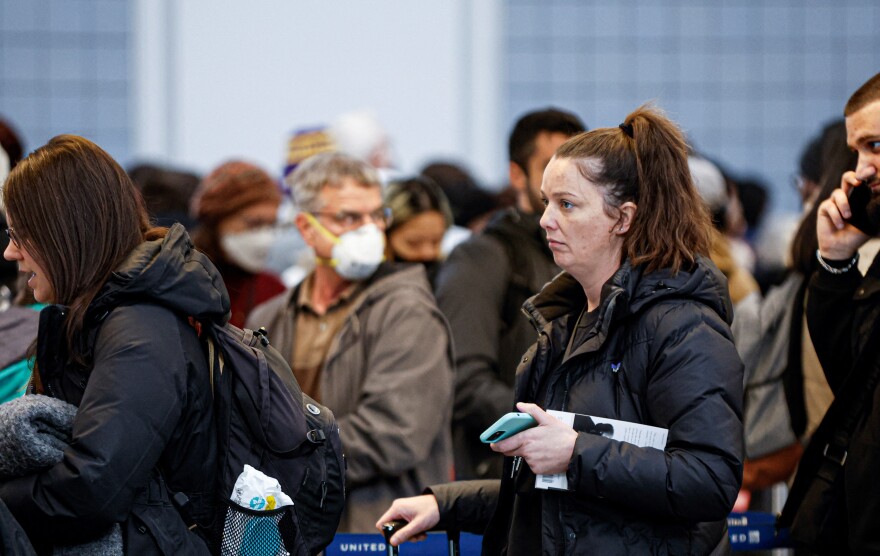 Travelers wait in line in coats, some in masks, many look disgruntled