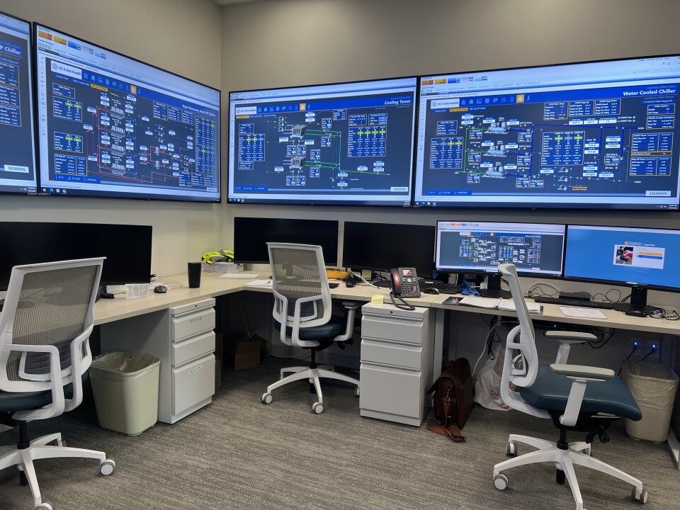 Large blue computer screens show activity over three desk and chairs. 