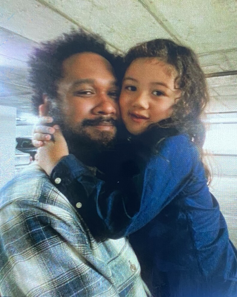 A man carries a young boy. The boy wraps his arms around the man's neck as they press their cheeks together.