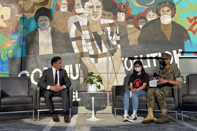 Under a mural featuring Karen Bass, the LA Unified superintendent talks with two masked students.