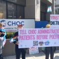 Protesters holding trans and LGBTQ+ pride flags pose for a photo outside Children Hospital of Orange County. Their signs say "Tell CHOC administration: Patients before politics," "Impeach, convict, and remove," and "Trust doctors."