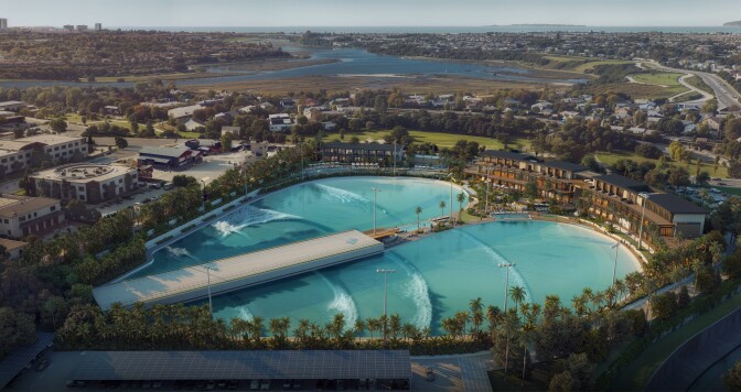 Two pools form a heart shape with a type of pier running down the middle of it: Uniform, generated waves are making their way across the surface. The exterior of the pools are lined with palm trees and building with patios where onlookers can catch the action.  