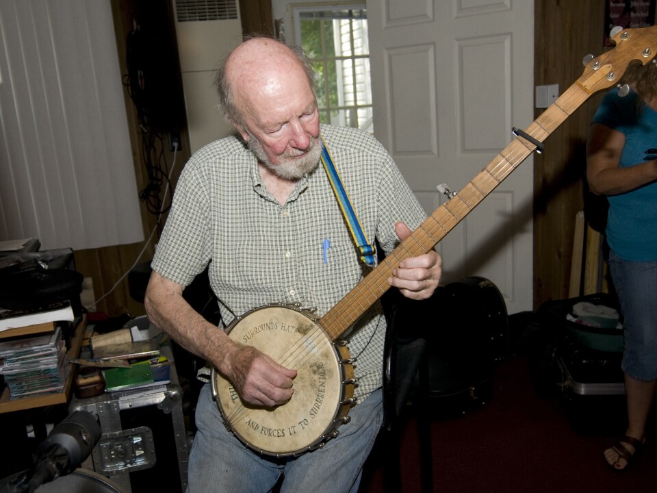 Seeger shows off his banjo, inscribed with the message, "This machine surrounds hate and forces it to surrender."