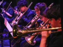 Students on a dimly lit stage play instruments while reading sheet music.