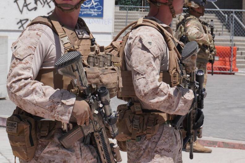 California national guard officers hold rifles while standing in front of a building with a fence.