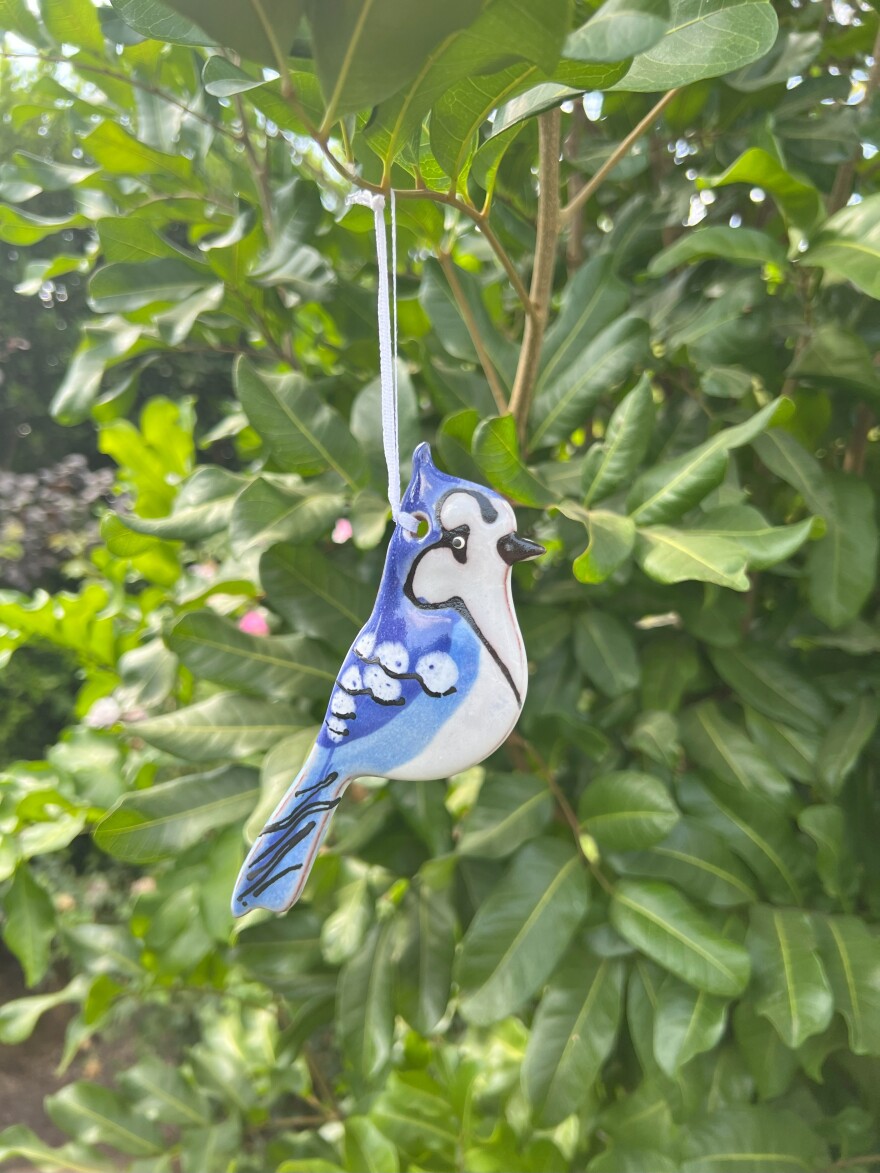 A hand crafted ceramic ornament depicting a blue jay hangs in a tree.