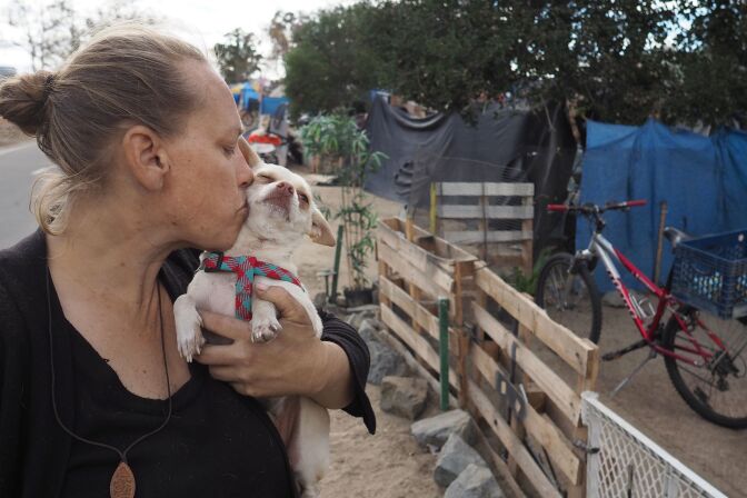 Homeless encampment resident Tammy Schuler kisses one of her pet dogs  beside a row of tents and tarps that line the Santa Ana River bicycle path, near Angel Stadium in Anaheim, California, January 25, 2018.  
People living along the riverbed recently learned they must pack their bags and move on, or risk arrest, but alternative housing options are limited. Urban development network CityNet says it has helped some 200 people get out of the street since July -- but the steady stream of new homeless people is relentless. / AFP PHOTO / Robyn Beck / TO GO WITH AFP STORY by Veronique DUPONT, "Faced with camp evacuation, California homeless live in fear"        (Photo credit should read ROBYN BECK/AFP/Getty Images)