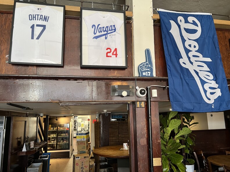 An Ohtani jersey, signed Robert Vargas jersey, and blue Dodgers flag are situated side by side above part of the interior of the"Far Bar".