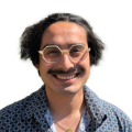 A person with medium-tone skin weat six-sided glasses and has a mustache.