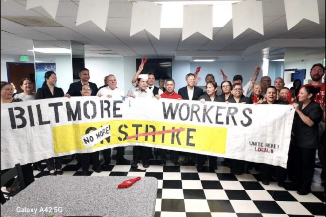 A crows of hotel workers gather behind a large banner with the words "Biltmore workers no more strike" as several in th ebackground raise their hands in celebration.