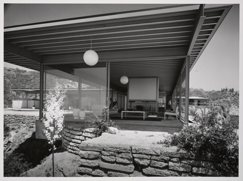 A black and white photo of a mid-century modern home taken from the outside looking into the living room. 