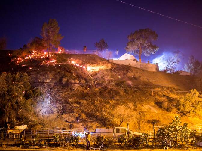 A woman takes a photo as the Creek Fire burns behind a hillside near houses in the Shadow Hills neighborhood of Los Angeles, California, on December 5, 2017.