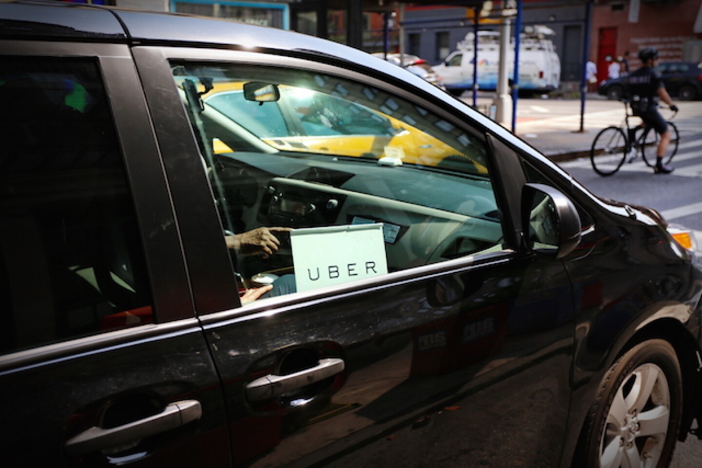 The front passenger side of a black car with a white Uber sign hanging in it is shown.