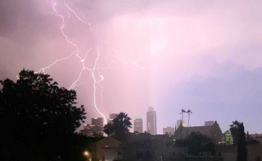 A lightning strike crackles across the sky, showing some downtown Los Angeles skyscrapers in the distance.