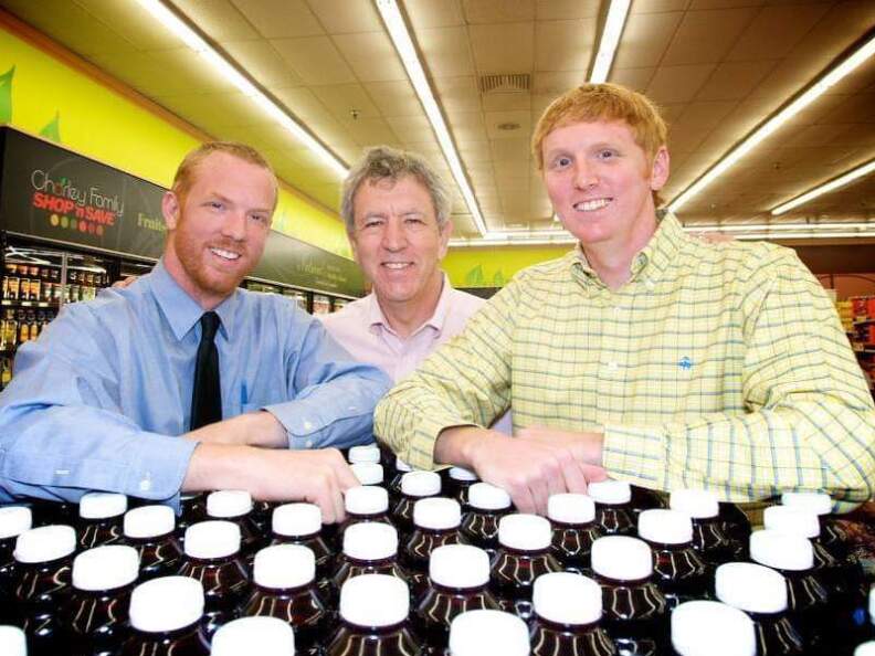 Three men pose for a picture leaning on a display of plastic bottles.
