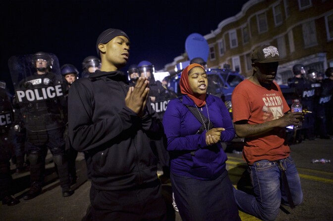 BALTIMORE, MD - APRIL 28:  Protestors say the Lord's Prayer beside riot police the night after citywide riots over the death of Freddie Gray on April 28, 2015 in Baltimore, Maryland. Freddie Gray, 25, was arrested for possessing a switch blade knife April 12 outside the Gilmor Houses housing project on Baltimore's west side. According to his attorney, Gray died a week later in the hospital from a severe spinal cord injury he received while in police custody. (Photo by Mark Makela/Getty Images)