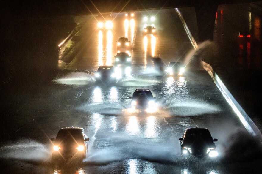Cars drive in the dark with their headlights, splashing through standing water on a roadway
