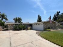 A gray house with a rock wall on either side. The house has a white garage door and has an American flag on a pole extending from the roofline. 