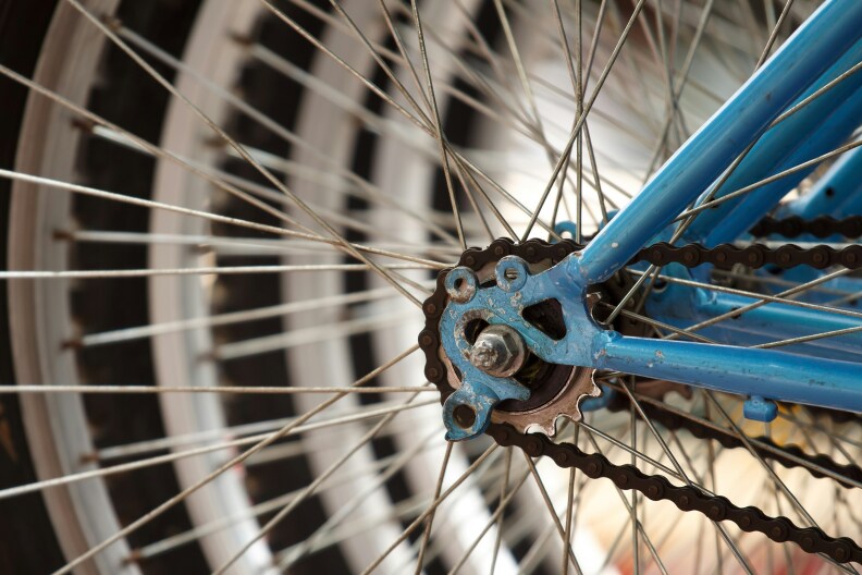 The wheel and chain for a blue bike, pictured close-up. Behind it, other bikes are parked next to just out of focus.