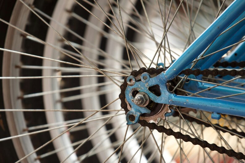 The wheel and chain for a blue bike, pictured close-up. Behind it, other bikes are parked next to just out of focus. 