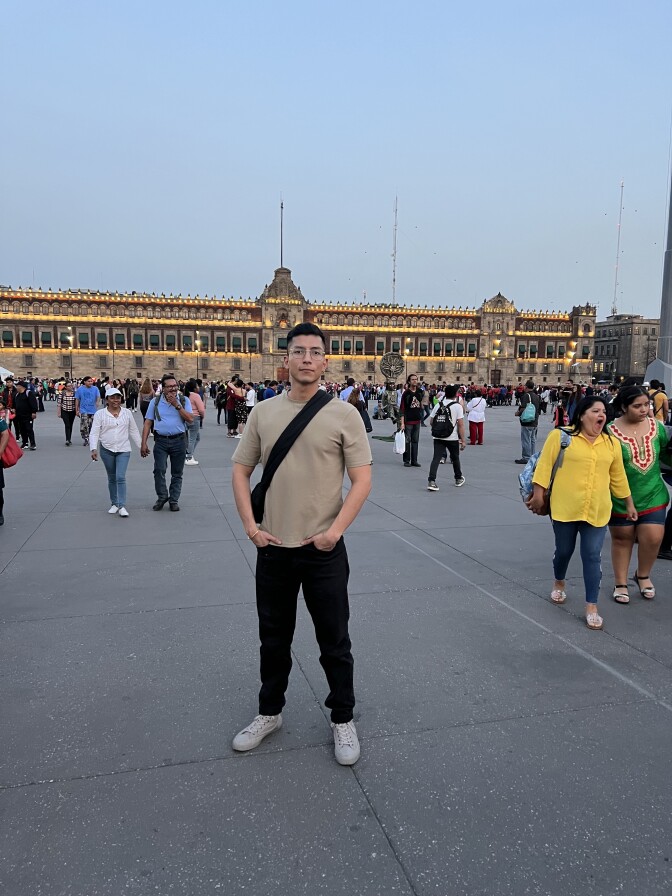 A light Brown man wearing glasses in front of Mexico City's Zocalo palace .