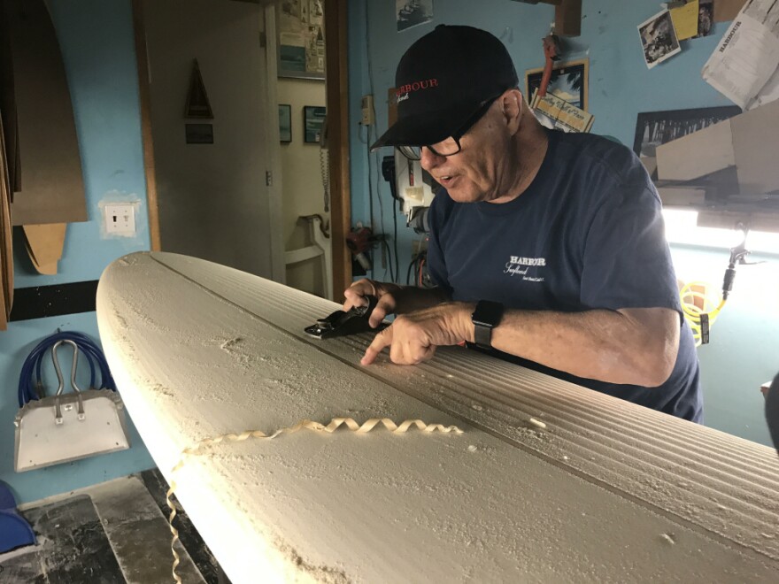 Rich Harbour in a ballcap and T-Shirt with his eponymous store name works on a surfboard by hand.