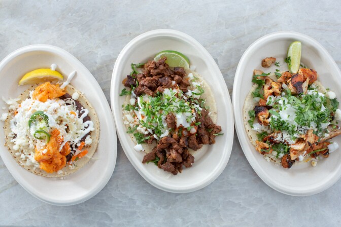 An aerial view of Que Padre tacos, a single taco of different varieties on three separate plates.