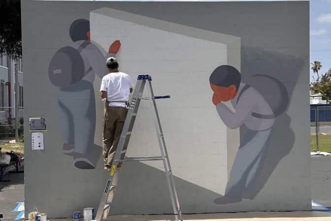Mural on brick wall depicting two people looking around a handball court wall.