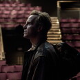Side profile view of Andrew Scott standing in an auditorium. Red seats can be seen in the background.