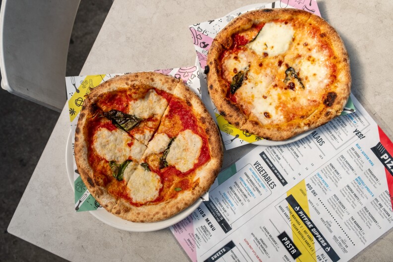 Two mini pizzas displayed on a table, with a Pitfire Pizza menu tucked just under the plates.